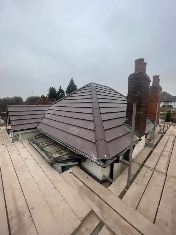 Re-tiled hipped roof with two brick chimneys, scaffold boards in the foreground